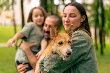Foto de Retrato feliz joven familia en parque con perro papá celebración hija en brazos concepto confianza cuidado y familia valores - Imagen libre de derechos