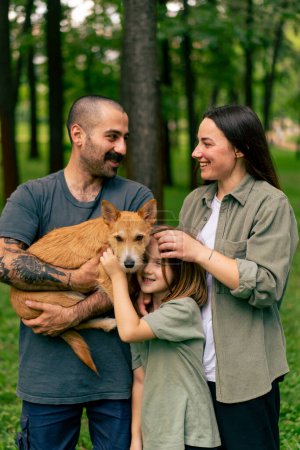 Téléchargez les photos : Portrait de jeune famille heureuse dans le parc avec chien papa maman fille repos concept confiance soins et valeurs familiales - en image libre de droit