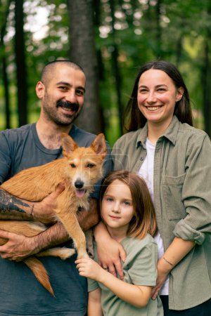 Photo for Portrait of happy young family in park with dog dad mom daughter resting concept trust care and family values - Royalty Free Image