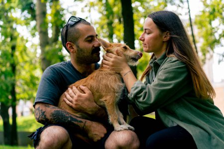 Téléchargez les photos : Portrait d'un jeune couple amoureux marchant dans le parc avec leur animal de compagnie l'embrassant amour chiens soins romance - en image libre de droit
