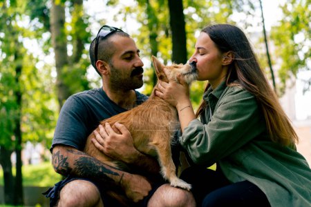 Téléchargez les photos : Portrait d'un jeune couple amoureux marchant dans le parc avec leur animal de compagnie l'embrassant amour chiens soins romance - en image libre de droit