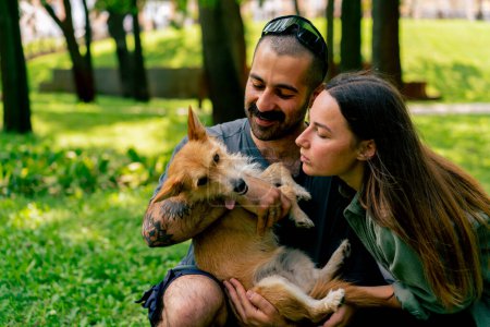 Foto de Retrato de una joven pareja enamorada caminando en el parque con su mascota besándolo amor perros cuidado romance - Imagen libre de derechos