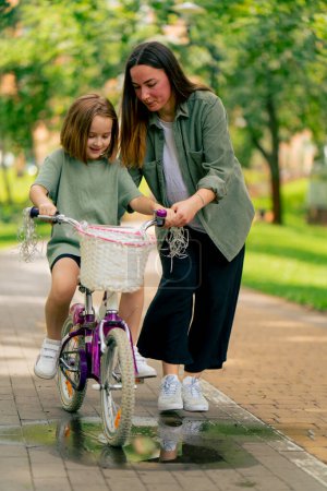 Foto de Retrato familia joven madre enseñando hija a montar en bicicleta en ciudad parque concepto feliz infancia y cuidado - Imagen libre de derechos