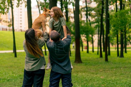 Foto de Feliz joven familia en parque con perro papá sosteniendo hija en brazos concepto de confianza cuidado y valores familiares - Imagen libre de derechos