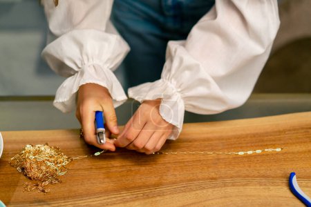 Téléchargez les photos : Mains rapprochées d'une jeune fille fait des bijoux avec ses propres mains coupe les restes de fil pour collier avec pinces production artisanale - en image libre de droit