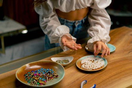 Téléchargez les photos : Gros plan de mains féminines fille créative aiguille choisit perles bracelet bijoux artisanal - en image libre de droit
