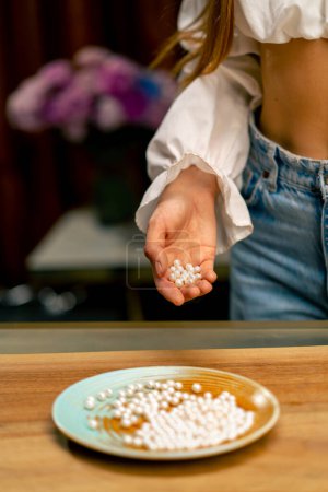 Téléchargez les photos : Gros plan de la main d'une femme versant des perles de perles blanches sur le plateau avant de commencer la production de bijoux artisanaux - en image libre de droit
