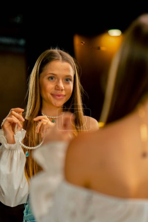 Téléchargez les photos : Portrait d'une jeune belle aiguille essayant sur un collier de perles se montrant dans la production artisanale miroir passe-temps beauté - en image libre de droit