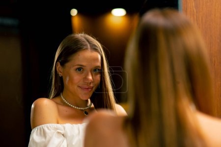 Téléchargez les photos : Portrait d'une jeune belle aiguille essayant sur un collier de perles se montrant dans la production artisanale miroir passe-temps beauté - en image libre de droit