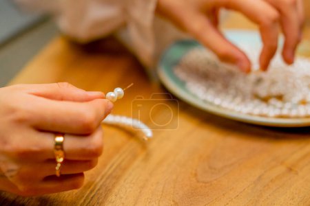 Foto de Las manos de cerca de una joven hace joyas con sus propias manos cuerdas cuentas en un alambre para el pasatiempo collar - Imagen libre de derechos