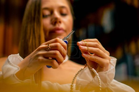 Foto de Primer plano una joven hermosa niña hace joyas con sus propias manos corta los restos de alambre para collar con alicates producción artesanal - Imagen libre de derechos