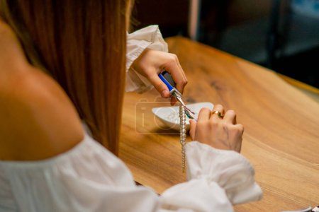 Téléchargez les photos : Mains rapprochées d'une jeune fille fait des bijoux avec ses propres mains coupe les restes de fil pour collier avec pinces production artisanale - en image libre de droit