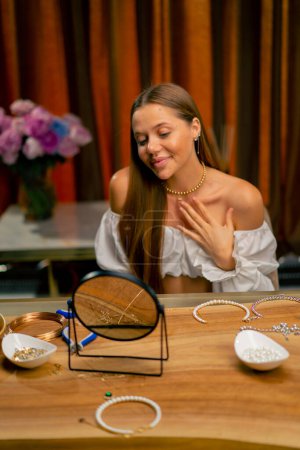 Photo for Portrait of a young beautiful needlewoman trying on a pearl necklace flaunting herself in mirror craft production hobby beauty - Royalty Free Image