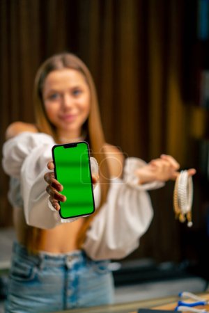 Foto de Retrato de una hermosa joven costurera sosteniendo un teléfono con una pantalla verde y muchos collares producción artesanal hobby trabajo en casa - Imagen libre de derechos