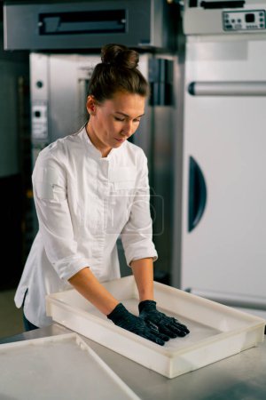 Photo for Professional female baker carefully kneads the dough for baking fresh bread in a cozy bakery - Royalty Free Image