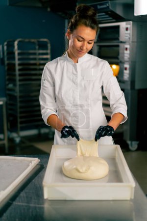 Foto de Panadero femenino profesional amasa cuidadosamente la masa para hornear pan fresco en una panadería acogedora - Imagen libre de derechos