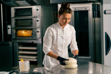 Foto de Panadero femenino profesional amasa cuidadosamente la masa para hornear pan fresco en una panadería acogedora - Imagen libre de derechos