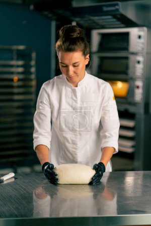 Photo for Professional female baker in the kitchen forms the dough into a perfect bread shape for sale in the bakery - Royalty Free Image