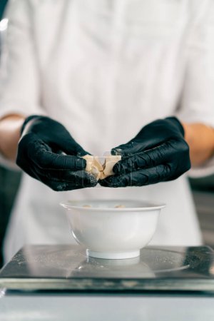 Foto de Primer plano de las manos femeninas en guantes rompiendo levadura para preparar la masa para hornear pan en una panadería - Imagen libre de derechos