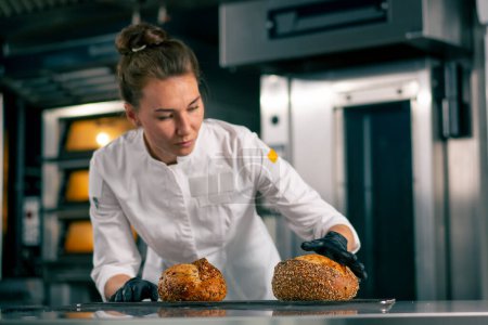 Photo for Close-up shot of freshly baked loaves of bread that a smiling girl cook places on a baking rack - Royalty Free Image