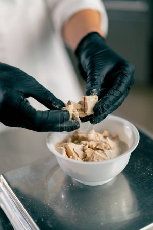 Photo for Close-up shot of female hands in gloves breaking yeast to prepare dough for baking bread in a bakery - Royalty Free Image
