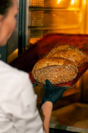 Téléchargez les photos : Plan rapproché de pain chaud fraîchement cuit debout sur une plaque de cuisson et en cours de finition au four sur - en image libre de droit