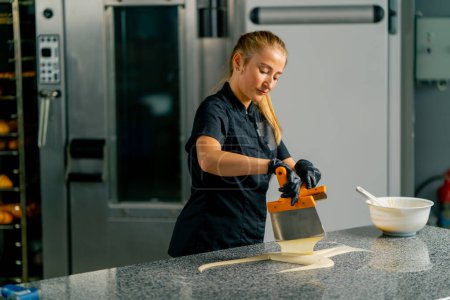 Photo for A girl pastry chef mixes melted white chocolate with a metal spatula on the table in a pastry shop for preparing desserts - Royalty Free Image