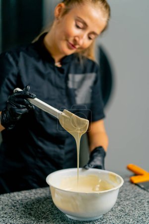 Téléchargez les photos : Fille chocolatier à l'aide d'une spatule en silicone mélange du chocolat pour faire des desserts dans une confiserie - en image libre de droit