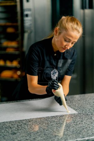 Photo for Using a pastry bag a girl pastry chef squeezes melted chocolate onto parchment to make natural sweets - Royalty Free Image