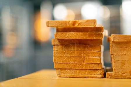 Foto de Primer plano de una hogaza de pan cortado en tostadas de pie sobre una tabla de madera en una superficie de cocina - Imagen libre de derechos
