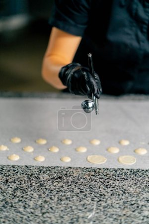 Foto de La mano femenina de un confitero en un guante utiliza un dispositivo especial para secar caramelos de chocolate en pergamino - Imagen libre de derechos