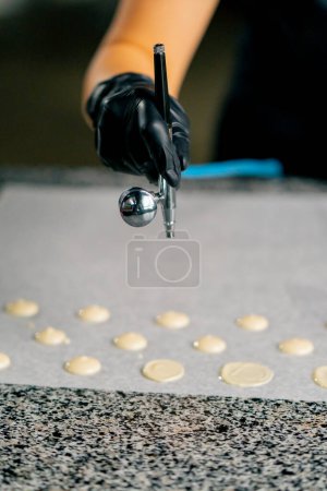 Foto de La mano femenina de un confitero en un guante utiliza un dispositivo especial para secar caramelos de chocolate en pergamino - Imagen libre de derechos