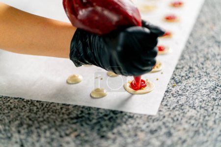 Photo for The gloved hand of a pastry chef squeezes the berry filling for natural chocolates out of a pastry bag - Royalty Free Image