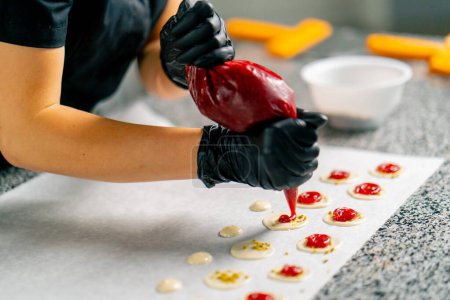Téléchargez les photos : La main gantée d'un chef pâtissier presse la garniture de baies pour les chocolats naturels dans un sac à pâtisserie - en image libre de droit