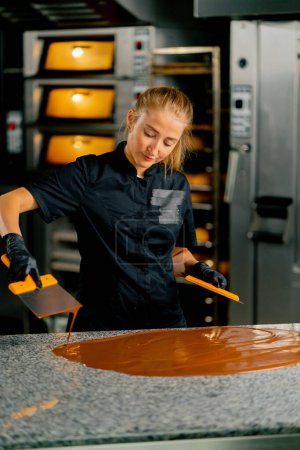 Téléchargez les photos : Un confiseur tempère le chocolat avant de préparer les desserts à l'aide d'une spatule métallique sur une surface de cuisine - en image libre de droit