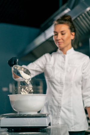 Photo for Female baker pours wheat flour into a mixer for kneading dough for preparing fresh baked goods - Royalty Free Image