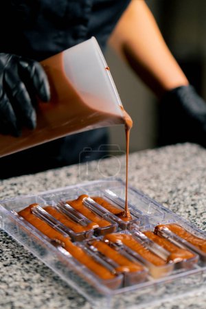 Photo for Melted hot chocolate is poured into a transparent chocolate mold for making natural candies in a confectionery shop - Royalty Free Image