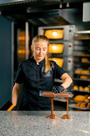Photo for A girl pastry chef pours hot melted chocolate into a chocolate mold for making natural sweets in a confectionery shop - Royalty Free Image