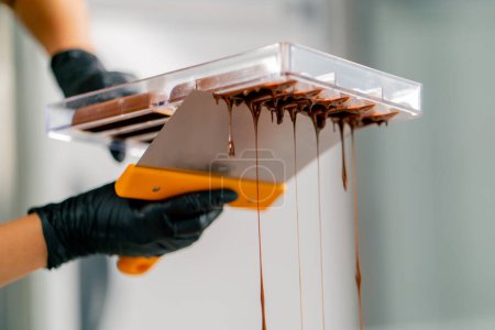 Téléchargez les photos : Gouttes de chocolat chaud fondu qui se déverse d'un moule inversé pour faire des bonbons dans une confiserie - en image libre de droit