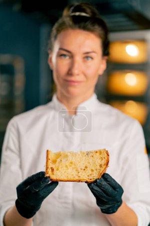 Foto de Retrato de una pastelera sonriente sosteniendo una hogaza de Pascua recién cortada con albaricoques secos y almendras pasas y mirando a la cámara - Imagen libre de derechos