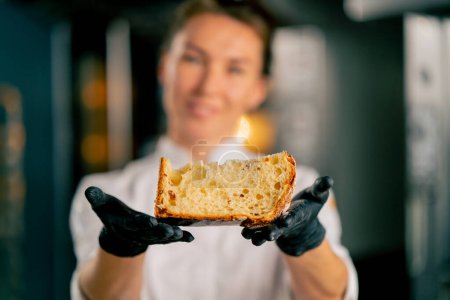 Photo for Portrait of a smiling female baker holding a freshly cut Easter loaf with raisins dried apricots and almonds and looking at the camera - Royalty Free Image