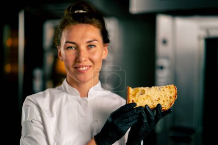 Téléchargez les photos : Portrait d'une pâtissière souriante tenant un pain de Pâques fraîchement coupé avec des raisins secs abricots et amandes et regardant la caméra - en image libre de droit