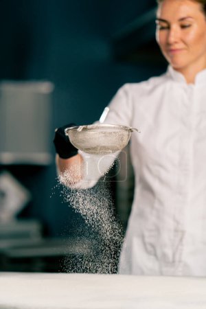 Foto de Primer plano de la mano de una cocinera tamizar harina a través de un tamiz en la superficie de la cocina - Imagen libre de derechos