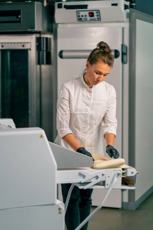 Téléchargez les photos : Femme boulanger met la pâte dans une machine spéciale pour dérouler la pâte avant de cuire des croissants frais - en image libre de droit