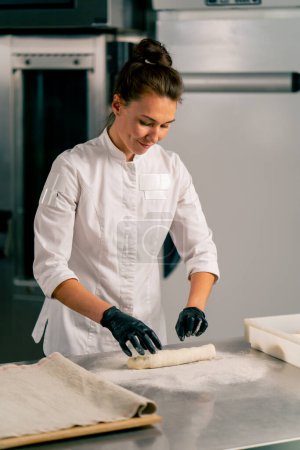 Téléchargez les photos : Femme boulanger concentré coupe la pâte en parts égales pour créer des formes croissant et les cuire - en image libre de droit
