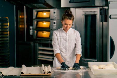 Téléchargez les photos : La boulangerie féminine concentrée roule la pâte en parts égales pour créer une forme de croissant avant la cuisson - en image libre de droit