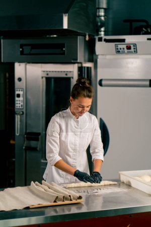 Foto de Rollos de panadero hembra concentrados masa en partes iguales para crear forma de croissant antes de hornear - Imagen libre de derechos