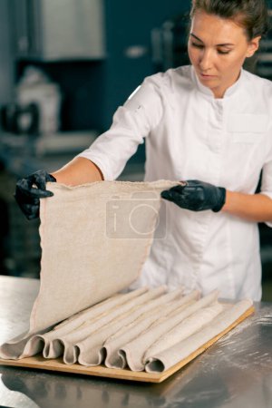 Téléchargez les photos : Gros plan sur les mains d'un chef et la pâte couchée dans la farine sur une surface de cuisine avant de former un croissant - en image libre de droit