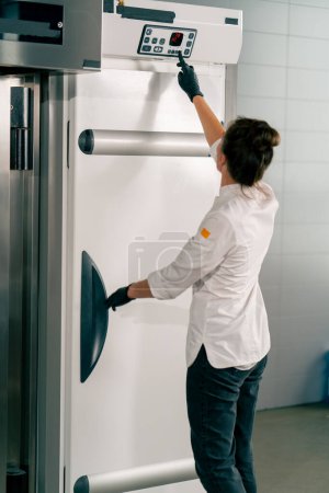 Foto de Una chica cocinera con su espalda a la cámara pone la masa en el refrigerador y establece la temperatura adecuada - Imagen libre de derechos
