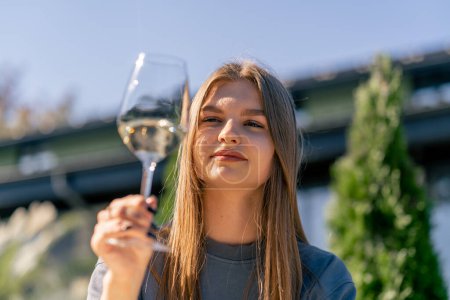 Téléchargez les photos : Gros plan d'une belle fille tenant un verre de vin à la main, inhalant son arôme et le dégustant sur la terrasse du jardin - en image libre de droit